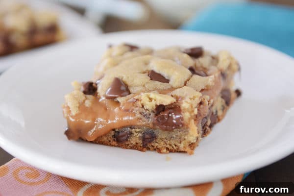 A single Peanut Butter Caramel Chocolate Chip Cookie Bar resting delicately on a white plate, highlighting its rich textures.