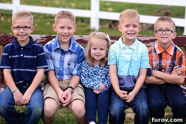 Five delightful children seated closely together on a rustic, weathered wooden bench, beaming at the camera.