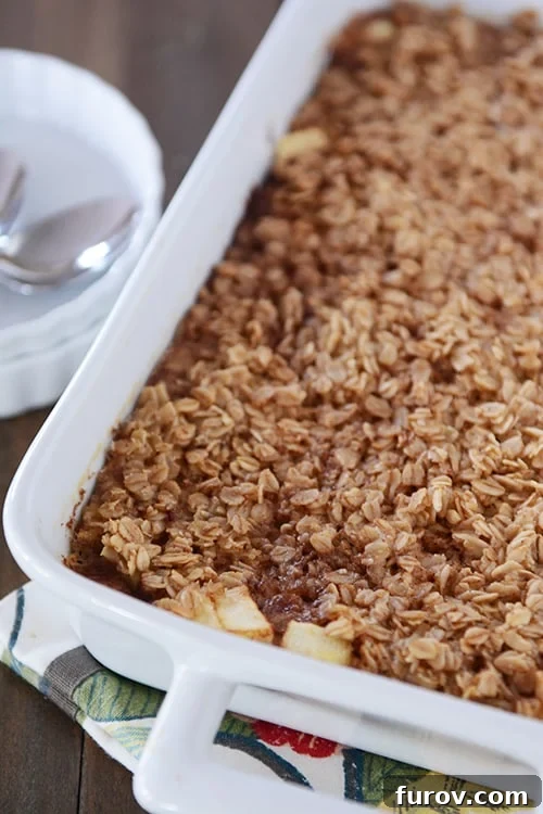 Old-Fashioned Apple Cinnamon Baked Oats 4 A white dish full of baked oatmeal with chunks of apple peeking out of the oatmeal at the front of the dish.