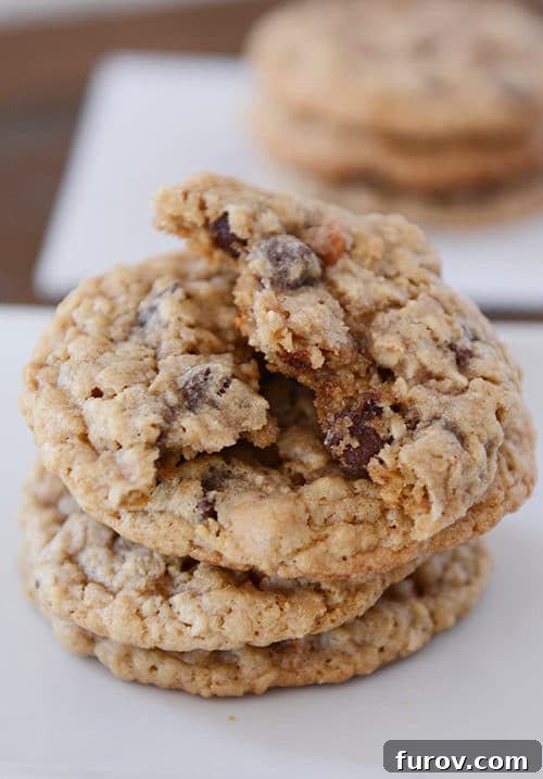 A stack of golden-brown oatmeal butterscotch chocolate chip cookies, with the top cookie expertly split in half to reveal its chewy interior and melted chips.