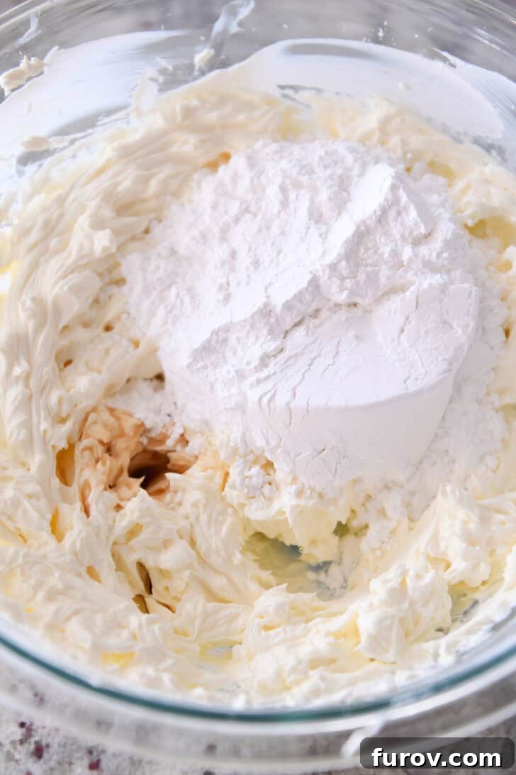 Ultimate No-Bake Cheesecake 3 Top down view of whipped cream cheese with flour on top in a glass bowl.