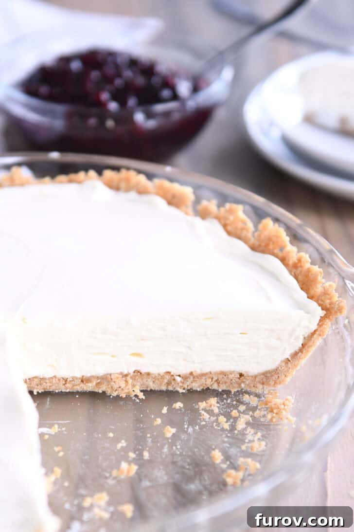 Ultimate No-Bake Cheesecake 8 A cheesecake with a graham cracker crust in a glass dish. A large slice is cut out of the cheesecake.