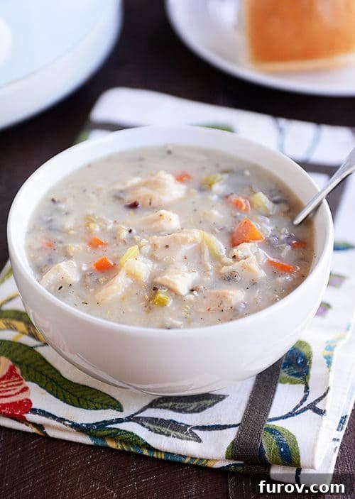 Slow Cooker Velvety Chicken and Wild Rice Soup 3 A white bowl full of creamy chicken, vegetable, and wild rice soup, garnished with fresh herbs, ready to be enjoyed.