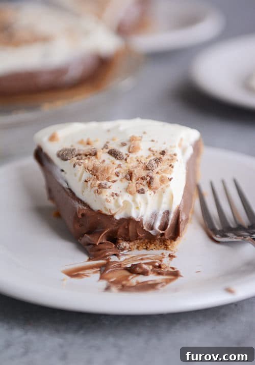 Slice of easy chocolate cream pudding pie with a graham cracker crust and whipped cream, a bite taken out, on a white plate.