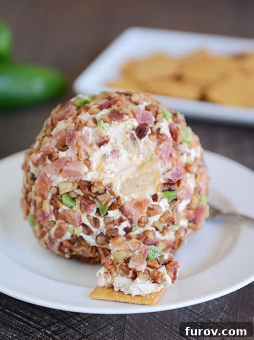 A bacon jalapeno cheeseball with a bite taken out on a cracker. The golden-brown bacon bits and vibrant green jalapeno pieces are visible, creating a tempting texture.
