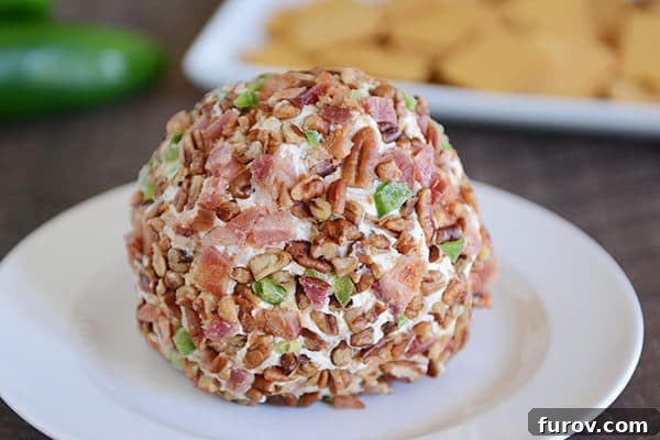 A meticulously crafted bacon, jalapeno, and nut covered cheeseball presented on a crisp white plate, showcasing its appealing texture and vibrant colors.
