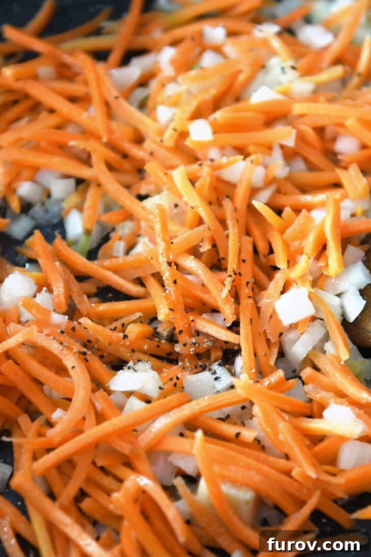 Top down view of matchstick carrots and onion being cooked in a skillet.