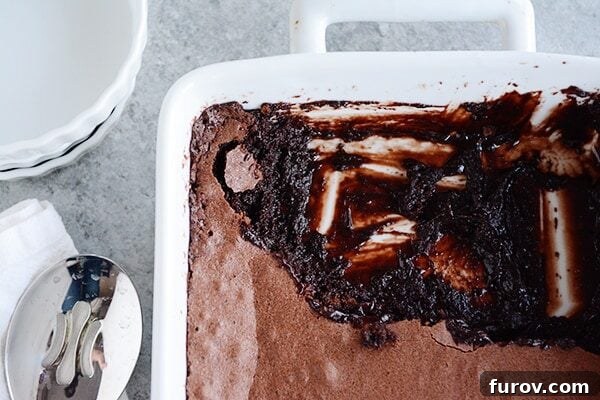 A white ceramic dish full of brownie pudding, with a portion scooped out, revealing its molten chocolate interior.