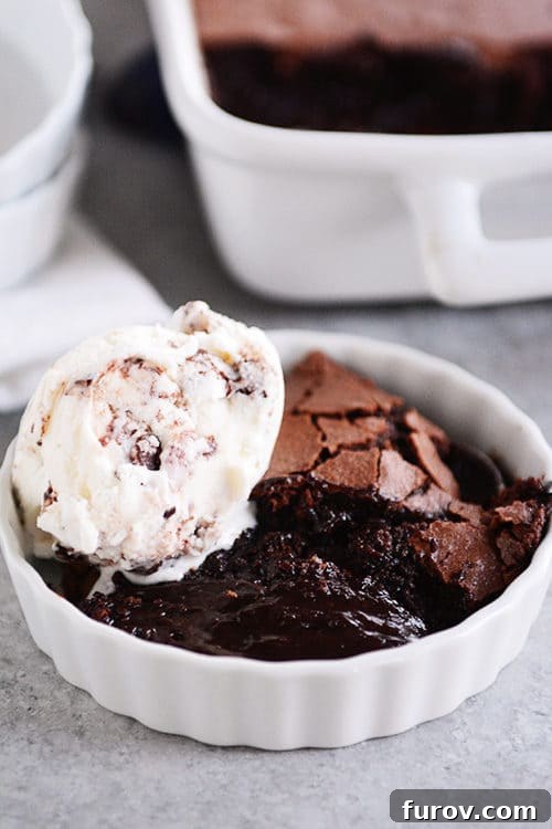 A white ramekin filled with brownie pudding, topped with a scoop of vanilla ice cream, ready to be enjoyed.