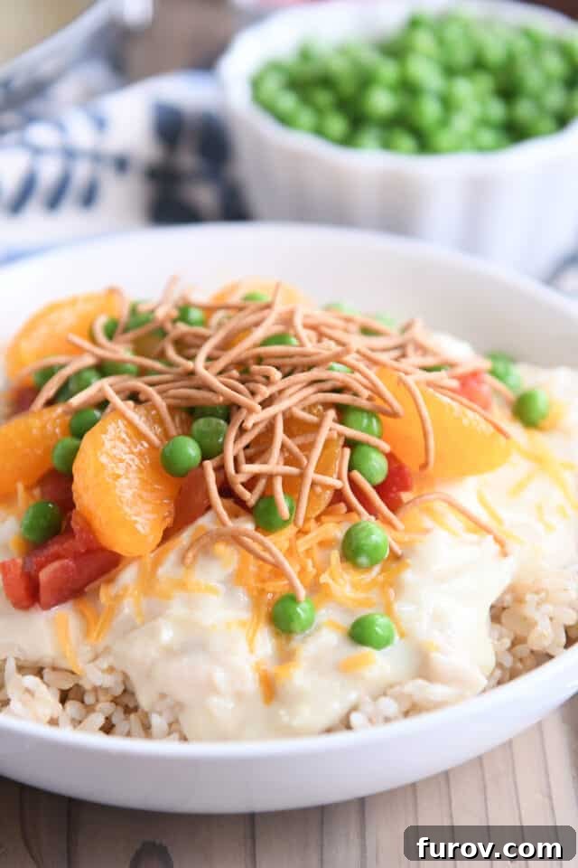 White bowl with rice, chicken gravy, peas, cheese, mandarin oranges and peas. A vibrant and appealing plate of Hawaiian Haystacks.