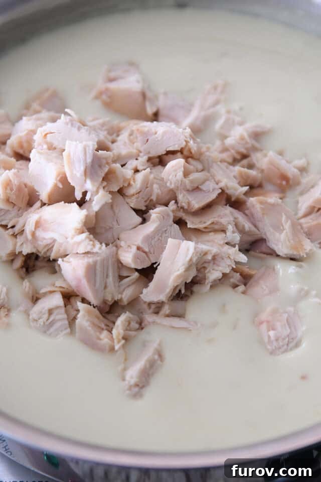 Cubed, cooked chicken stirred into a saucepan with white, creamy gravy.