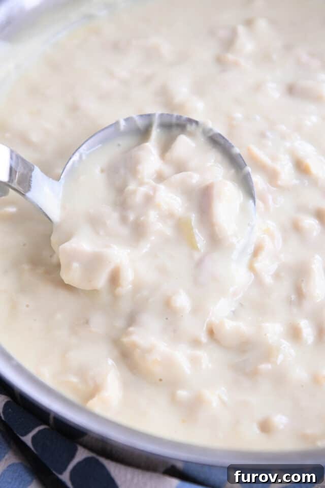Ladle scooping up a generous portion of thick, white chicken gravy, highlighting its creamy texture.