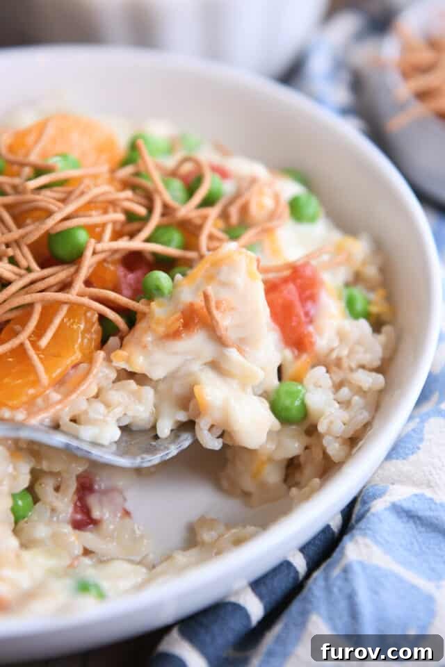 White shallow bowl with fork taking a bite of rice, chicken gravy, peas, and cheese. A close-up of a delightful mouthful.