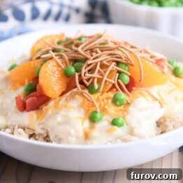 White bowl with brown rice, Hawaiian Haystacks gravy, mandarin oranges, chow mein noodles and peas. A complete and inviting Hawaiian Haystacks dish.