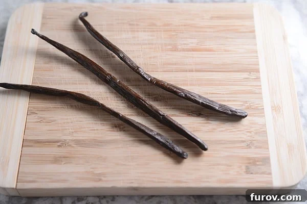 Three vanilla beans laying on a cutting board.