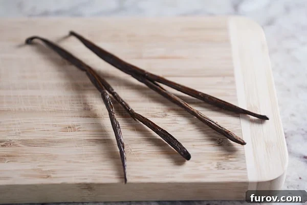 Four vanilla beans laying on a cutting board.
