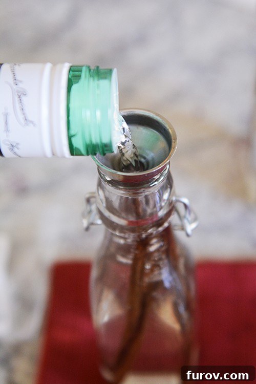 Alcohol getting poured into a glass bottle with vanilla beans.