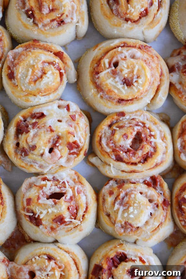 A cookie sheet filled with golden brown pepperoni pizza pinwheels, fresh from the oven, showcasing their swirled layers of dough, sauce, and cheese.