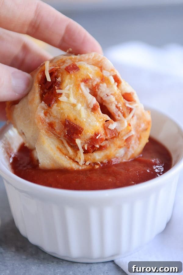 A perfectly cooked pepperoni pizza roll, with visible layers of melted cheese and pepperoni, being dipped into a bowl of vibrant marinara sauce.