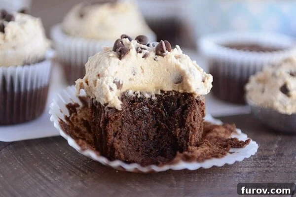 Double Fudge Brownie Cupcakes 3 A chocolate cupcake with a generous layer of cookie dough frosting, with a bite taken out to reveal the dense, fudgy interior.