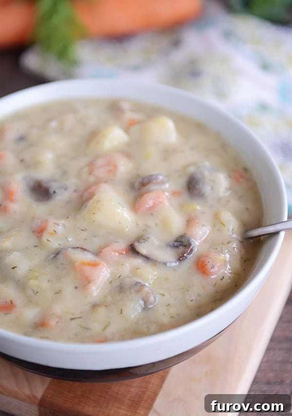 A white bowl of creamy mushroom, carrot, and potato soup, garnished with fresh dill.