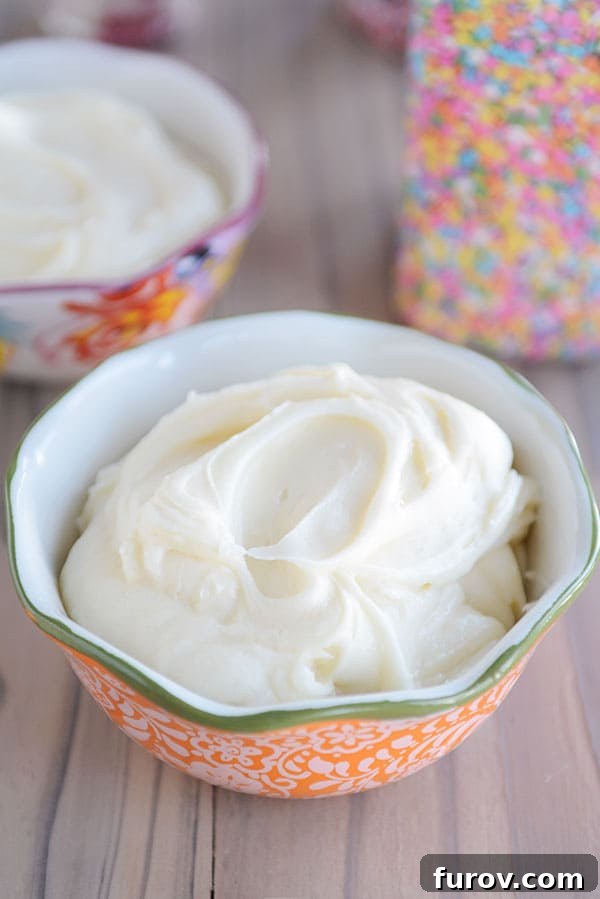 A large bowl brimming with fluffy, creamy vanilla buttercream frosting, with a jar of colorful sprinkles and another bowl of frosting in the soft focus background, suggesting delicious possibilities.