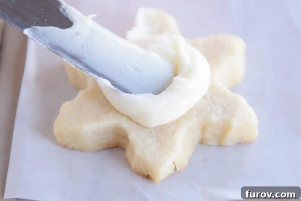 A metal offset spatula artfully spreading smooth, creamy buttercream frosting on a star-shaped sugar cookie, showcasing the perfect consistency for decoration.