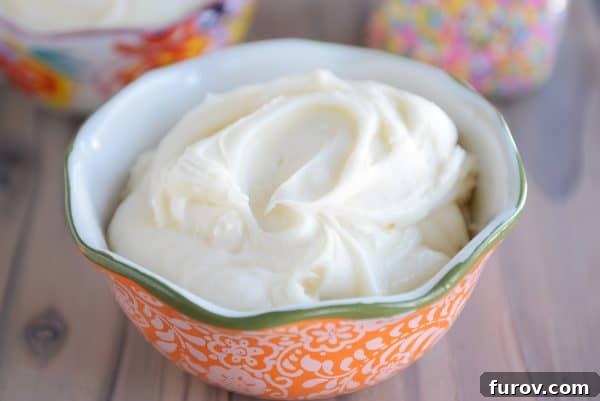 A vibrant orange bowl filled to the brim with smooth and glossy vanilla buttercream frosting, ready to be spread or piped.