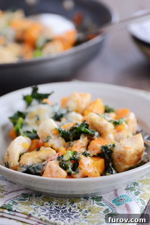 A bowl filled with cubed sweet potato, kale, cooked chicken, and melted cheese.