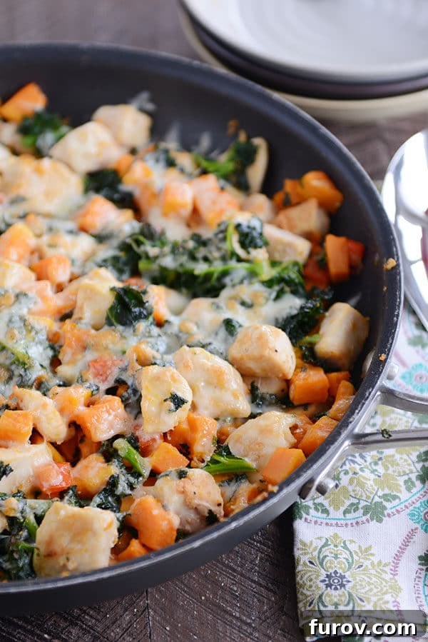 A skillet filled with cubed sweet potato, kale, cooked chicken, and melted cheese.