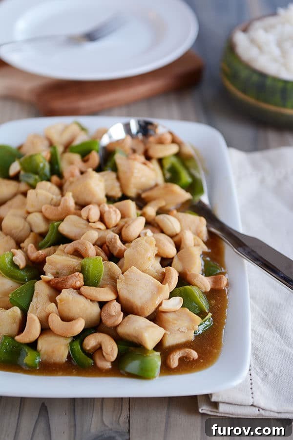 Quick Weeknight Chinese Cashew Chicken 4 A large metal spoon on a white tray of saucy chinese cashew chicken.