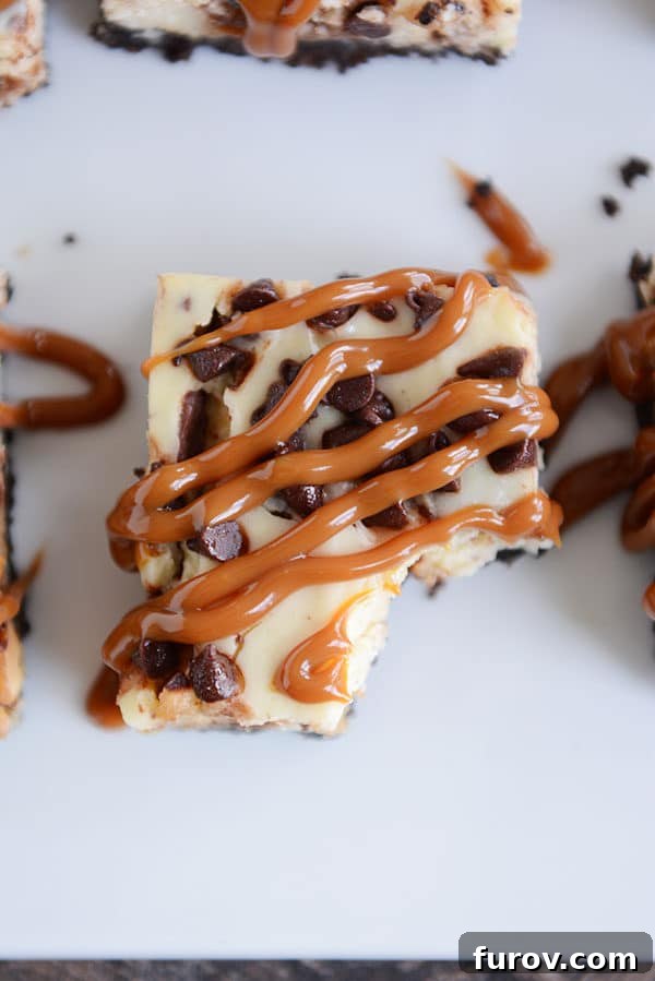 A top-down view of a decadent caramel cheesecake chocolate chip bar with a small bite taken out, revealing its rich, layered interior and tempting textures.