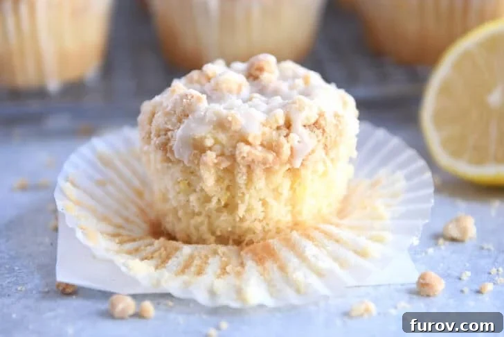 A lemon muffin topped with a crumb topping and white glaze sitting on a muffin liner.