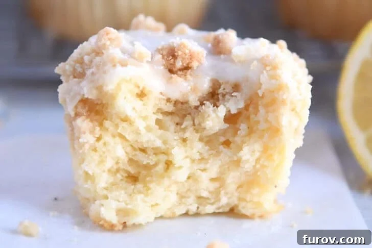 A half eaten lemon muffin with a crumb topping and white glaze.