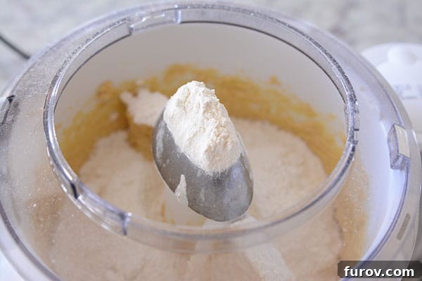 A mix of butter, flour, and sugar actively blending within the white bowl of a Bosch Universal stand mixer, highlighting its efficient mixing.