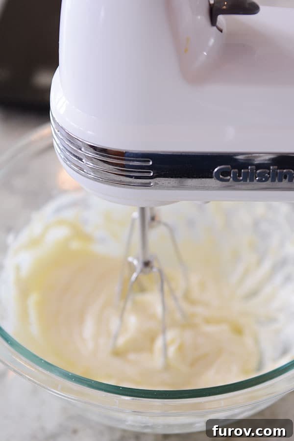 A handheld electric mixer actively whipping butter in a clear glass bowl, demonstrating its use for smaller tasks.