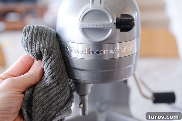 A kitchen rag meticulously wiping off a gleaming silver KitchenAid mixing bowl, showcasing its pristine condition.