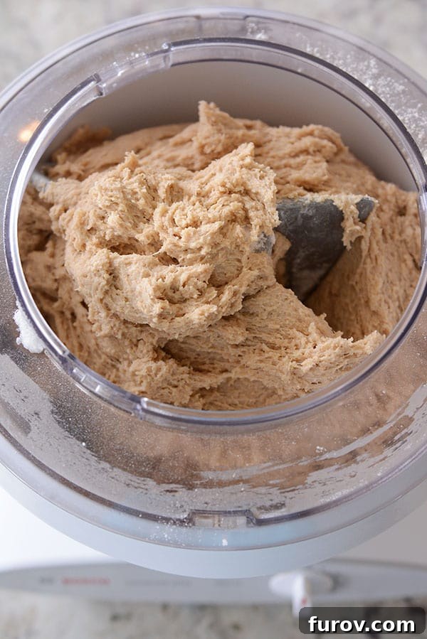 A large quantity of chocolate chip cookie dough being mixed in the spacious bowl of a Bosch stand mixer, demonstrating its capacity.