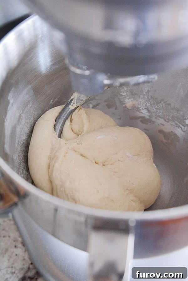 Bread dough actively mixing inside the stainless steel bowl of a red KitchenAid stand mixer, demonstrating its mixing action.
