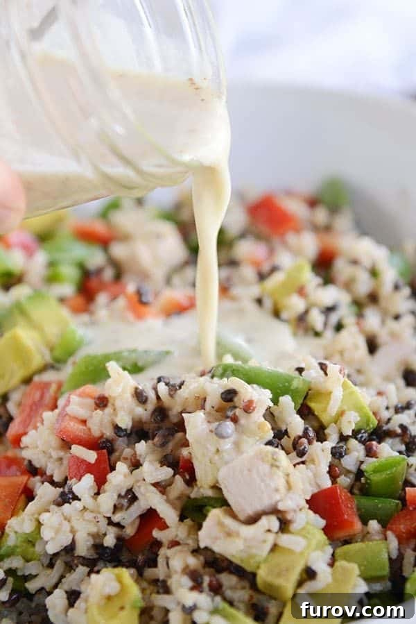 Dressing getting poured over a bowl of santa rosa chicken and wild rice salad.