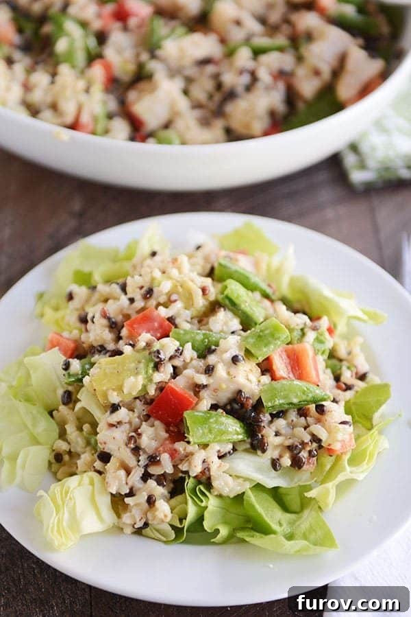 A white plate of green salad topped with a rice, tomato, and avocado mixture.