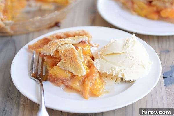 Juicy Fresh Peach Pie with Lattice or Crumb Topping 9 A delectable slice of peach pie with a fork, paired with a melting scoop of vanilla ice cream, on a pristine white plate.