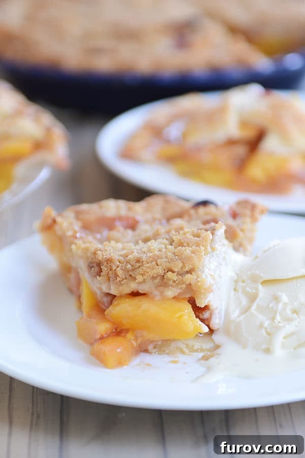 Juicy Fresh Peach Pie with Lattice or Crumb Topping 3 A generous slice of fresh peach pie with a golden crumb topping and a scoop of melting vanilla ice cream on a white plate.
