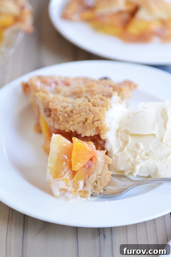 Juicy Fresh Peach Pie with Lattice or Crumb Topping 6 A fork taking a bite from a slice of fresh peach pie, artfully placed beside a scoop of vanilla ice cream.