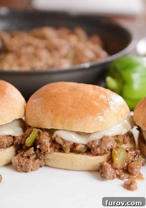 Philly cheesesteak sloppy joes served in buns, with a skillet of sloppy joe meat in the background.