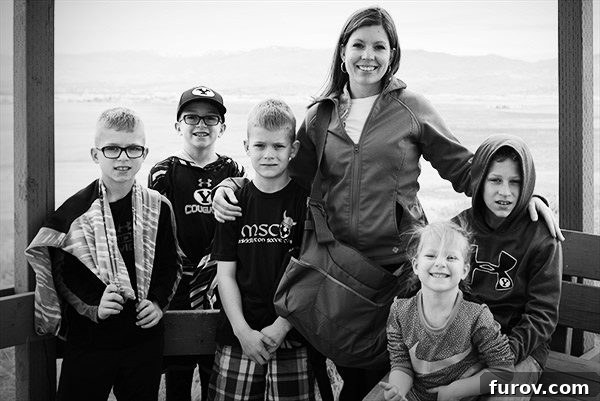 A mom standing with her five kids in front of a big window, sharing a warm family moment.