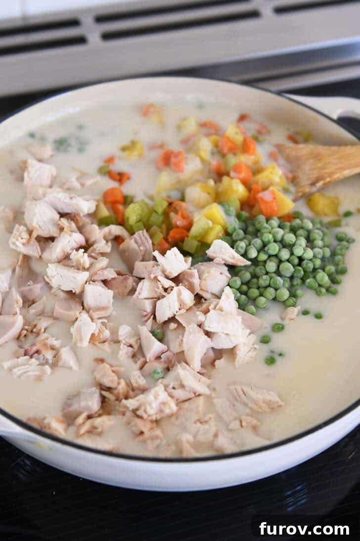 The Perfect Chicken or Turkey Pot Pie 4 Cast iron pan filled with white sauce, cooked chicken, peas, potatoes, carrots and celery.