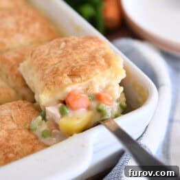 Spoon lifting out scoop of chicken pot pie filing for white 9X13-inch pan with baked biscuit on top.