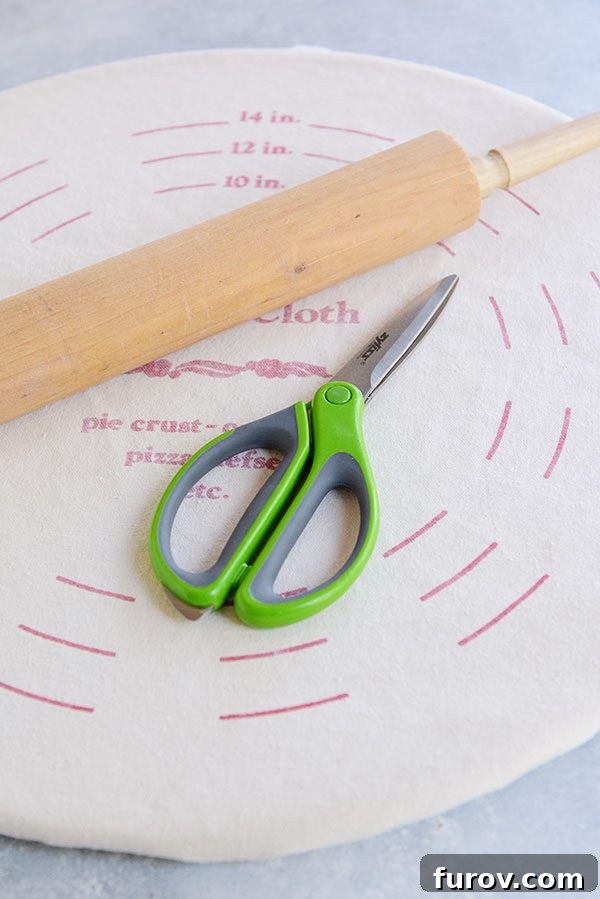 Kickstart Your Pie Making: Essential Tools and Ingredients 6 Kitchen shears and a wooden rolling pin resting on a pie crust pastry cloth, useful tools for dough preparation.