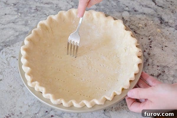 A fork poking holes in the bottom of an uncooked pie crust.